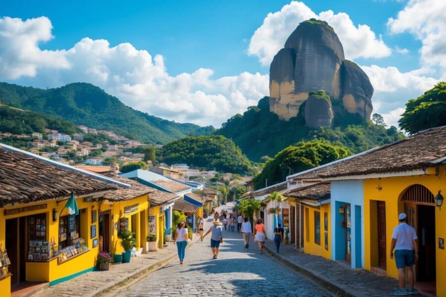 Vista panorâmica de São Thomé das Letras com casas coloridas, pessoas caminhando e formações rochosas ao fundo sob céu azul.